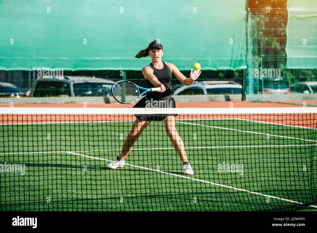 Teenage girl recieving a tennis ball with a volley counter shot. Practicing on a brand new outdoor tennis court. Vibrant green and brown with clear wh Stock Photo