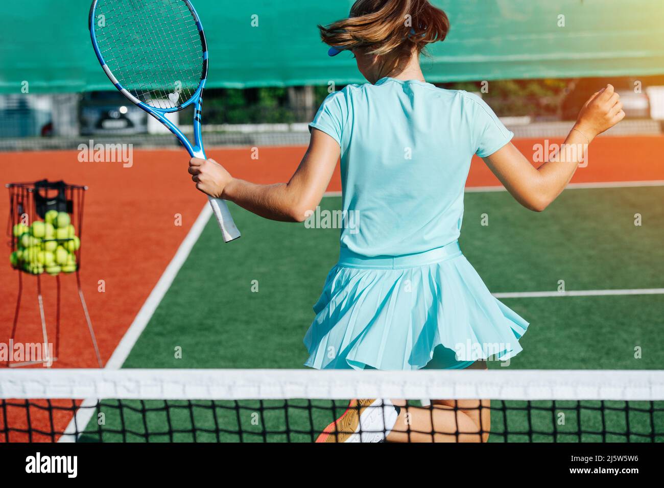 Back view of a carefree light teenage girl turning around in her short tennis skirt. Vibrant green and brown with clear white lines. Stock Photo