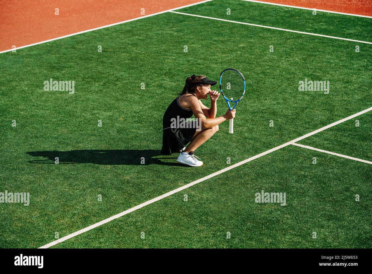 Crouched laughing girl during practice on a brand new outdoor tennis court. Vibrant green and brown with clear white lines. Stock Photo