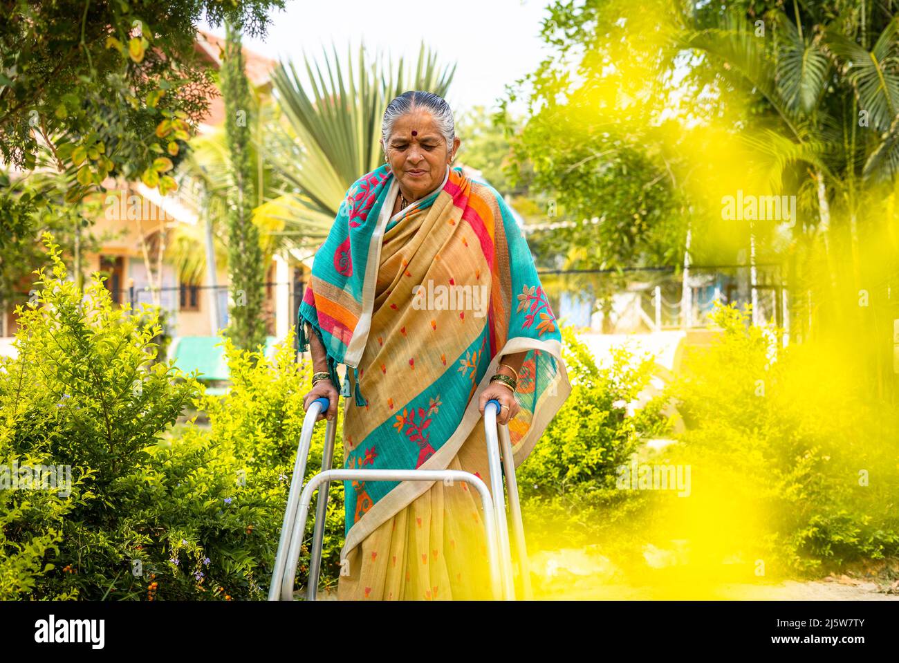 old woman walking with support of walker due to knee joint pain at park