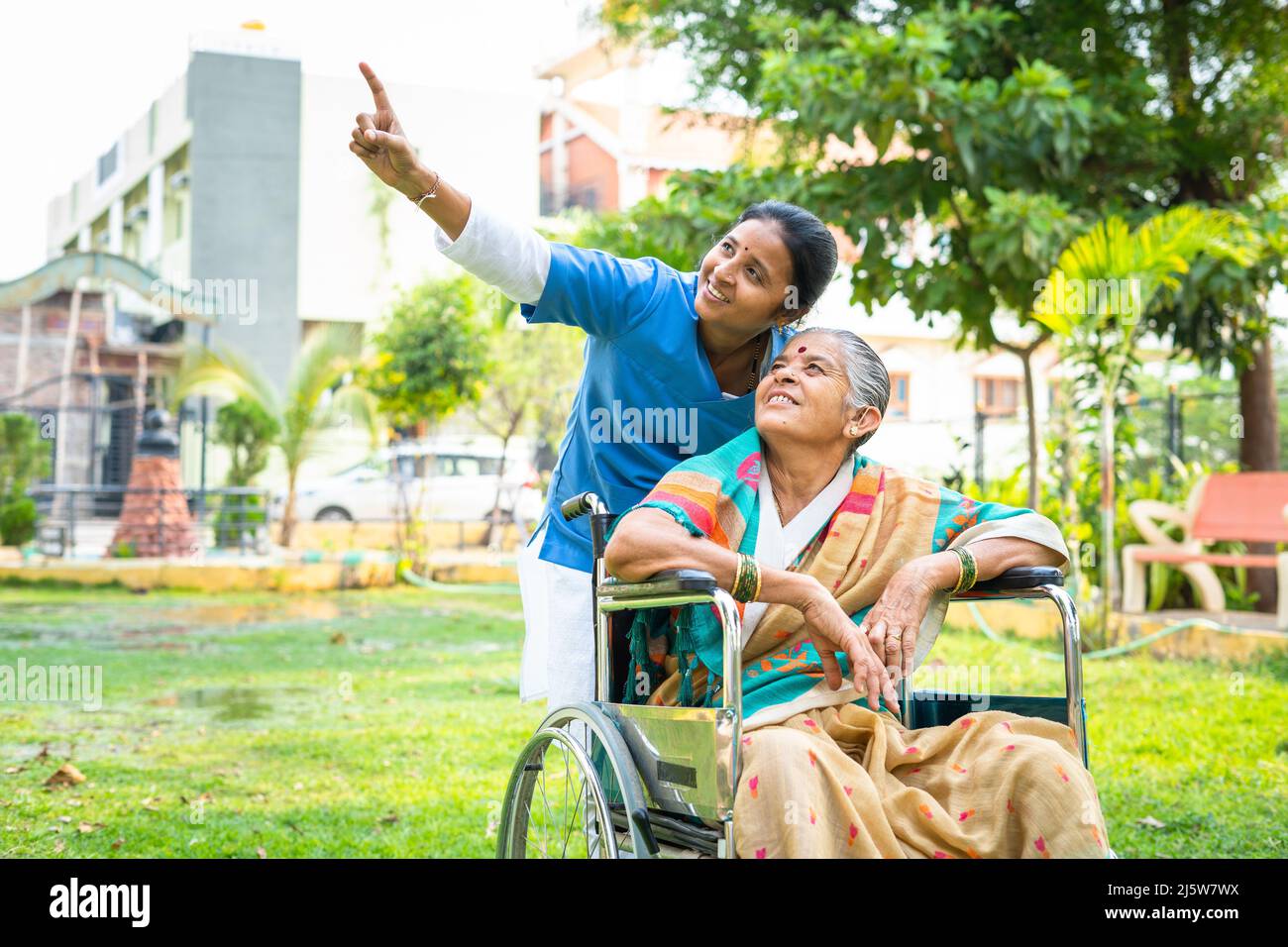 Nurse showing nature and birds to senior women while sitting on wheelchair at park - concept of relaxation, healthcare treatment and rehabilitation. Stock Photo