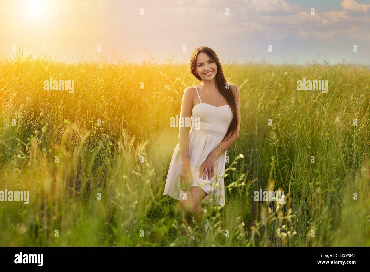 Beautiful young woman in white tank top and skirt dancing in the field under vibrant sunset Stock Photo