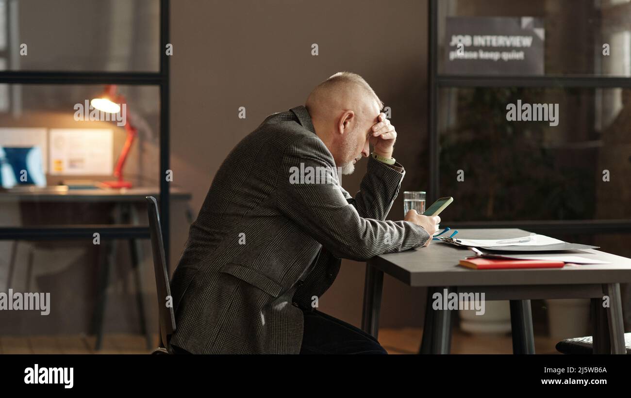 Mature man using his mobile phone at table while waiting for interviewer during job interview Stock Photo