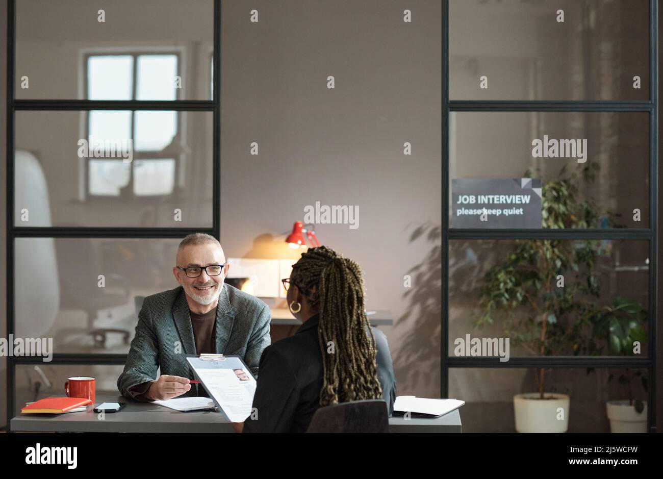 Mature manager in eyeglasses smiling to candidate during presentation of her resume at table at