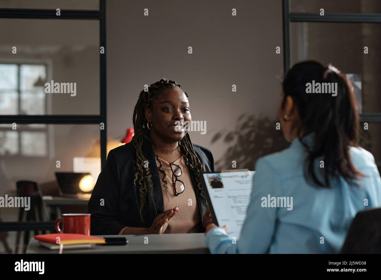 African young woman talking about her work experience to interviewer while they sitting at table during job interview Stock Photo