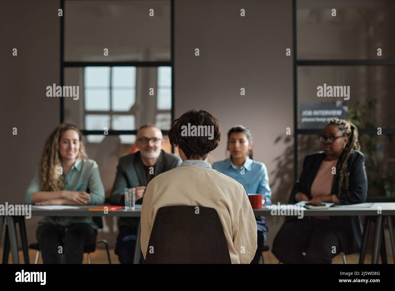 Rear view of young man sitting on chair opposite business people who ...