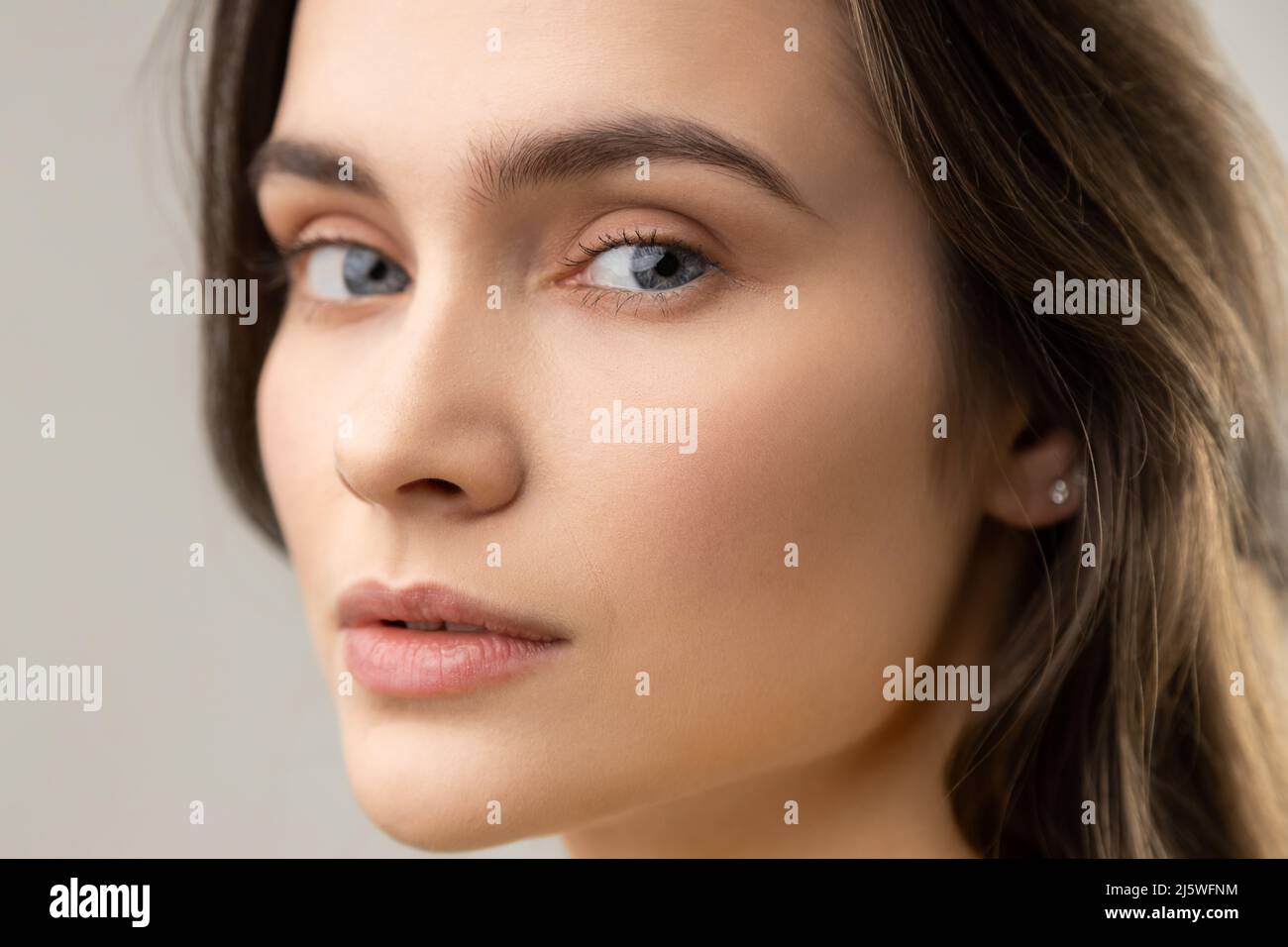 Closeup beauty portrait of beautiful woman with perfect skin, looking at camera with calm expression, wearing casual style jacket. Indoor studio shot isolated on gray background. Stock Photo