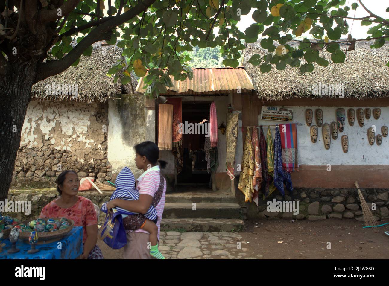 Women having conversation in a background of a house door, where traditional clothes and arts are hanged, in the traditional village of Tenganan Pegringsingan in Karangasem, Bali, Indonesia. Stock Photo