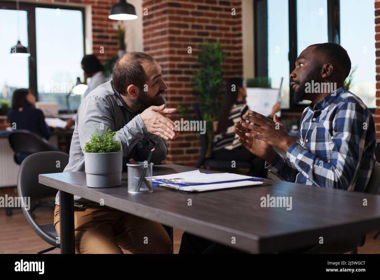 HR department head manager trying to calm down irritated job applicant while sitting at desk in office space. Upset employer arguing with agitated man about job high requirements. Stock Photo