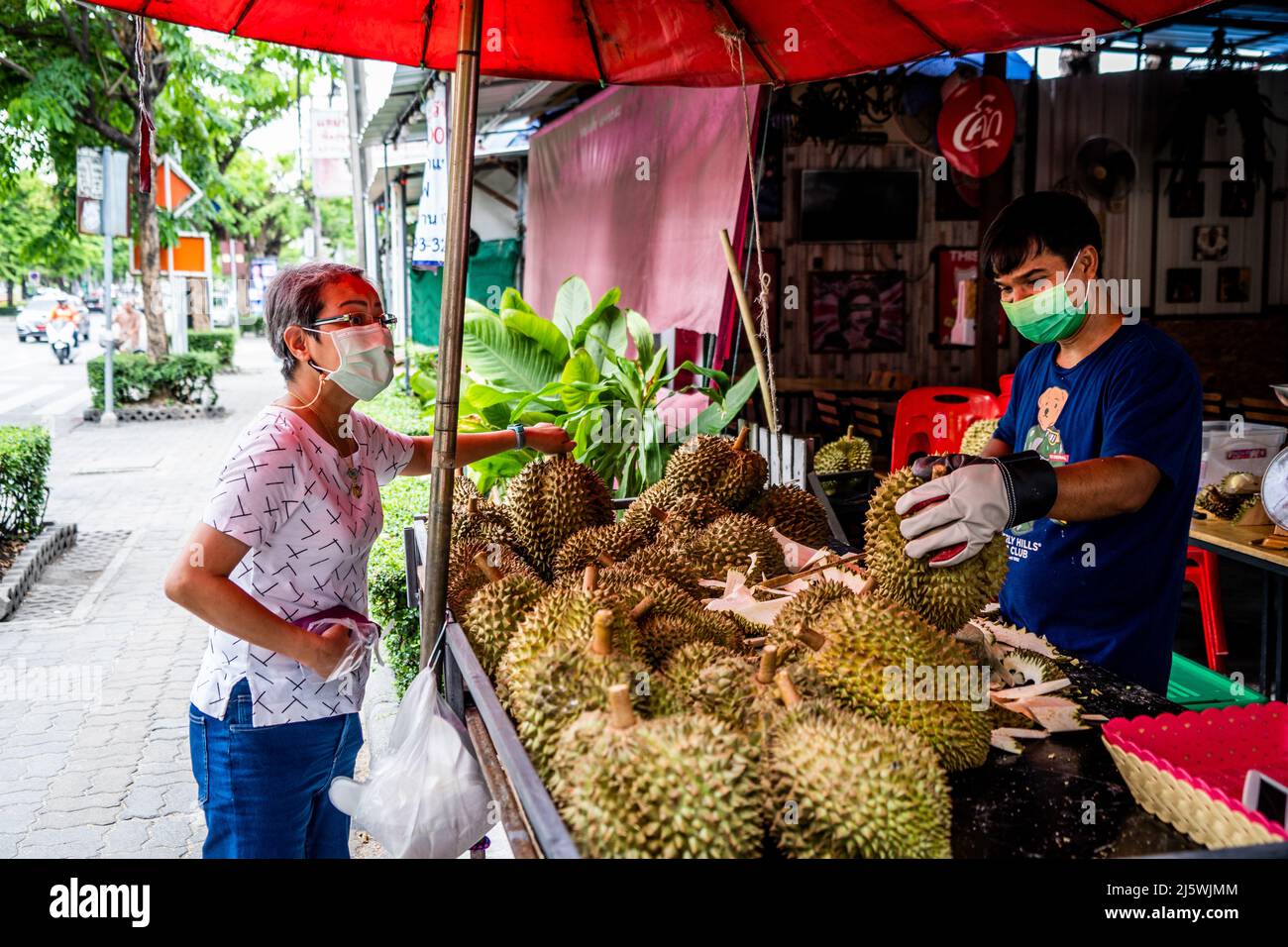 A durian vendor helps a customer to select their product at an outdoor market. Durian season