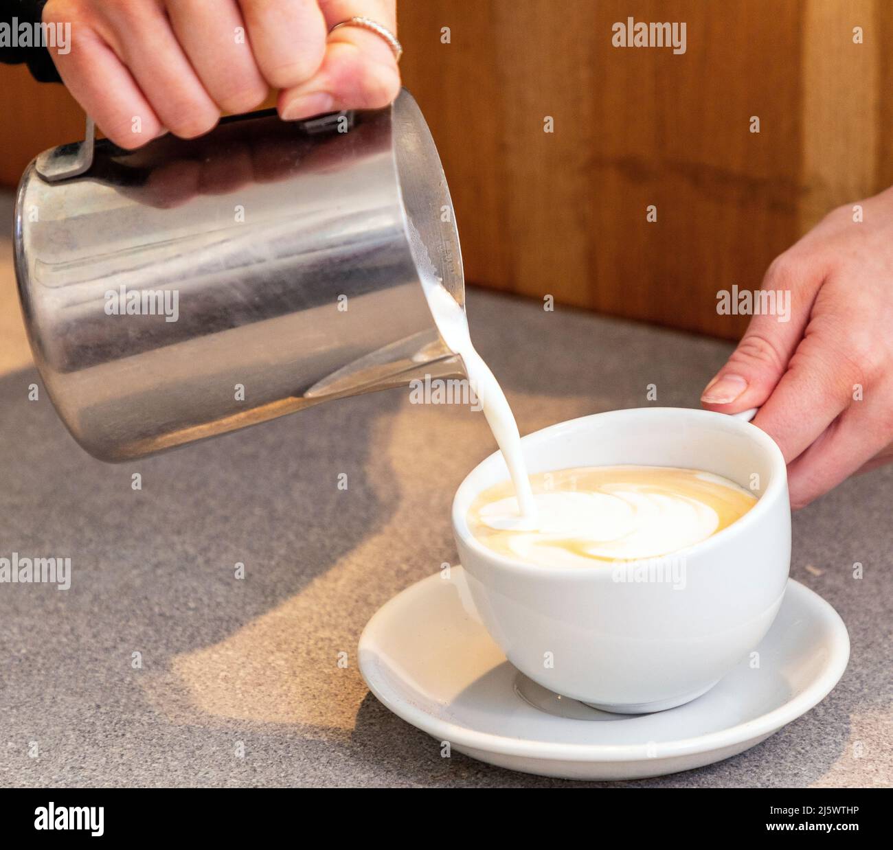 Pouring hot frothy milk into a coffee to make a latte Stock Photo