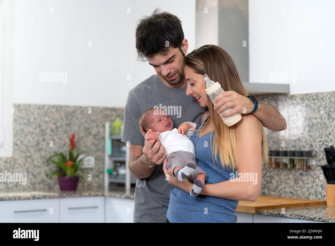 mother and father bottle feeding their newborn baby in the kitchen Stock Photo
