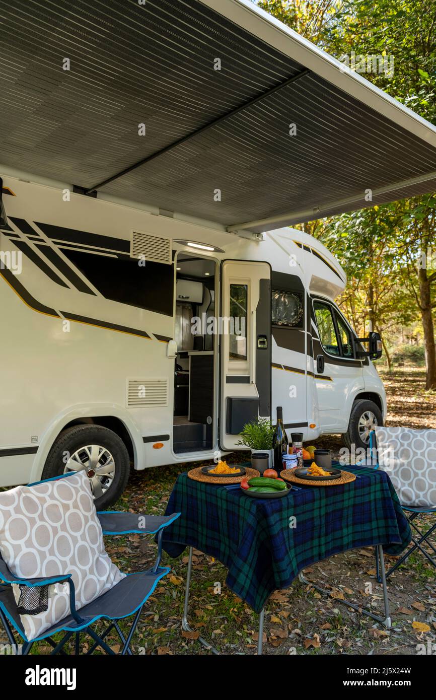 Motor home at campsite with a table and chairs set up outside the vehicle and ready to eating and drinking. Stock Photo