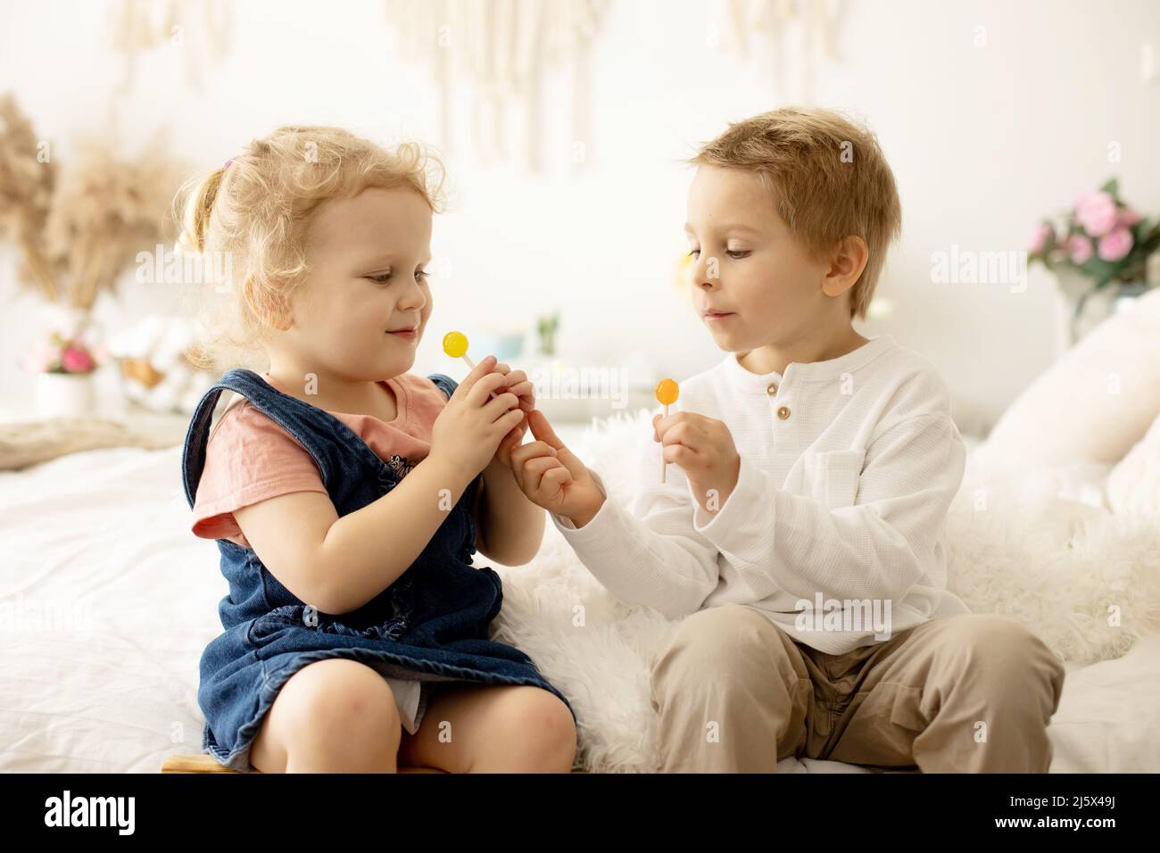 Cute toddler children, boy and girl, eating lolly pop at home, enjoying
