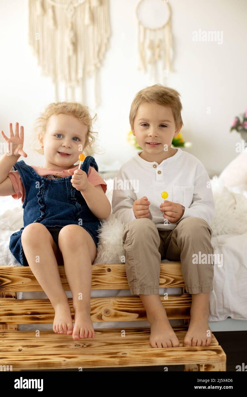 Cute toddler children, boy and girl, eating lolly pop at home, enjoying sweets Stock Photo