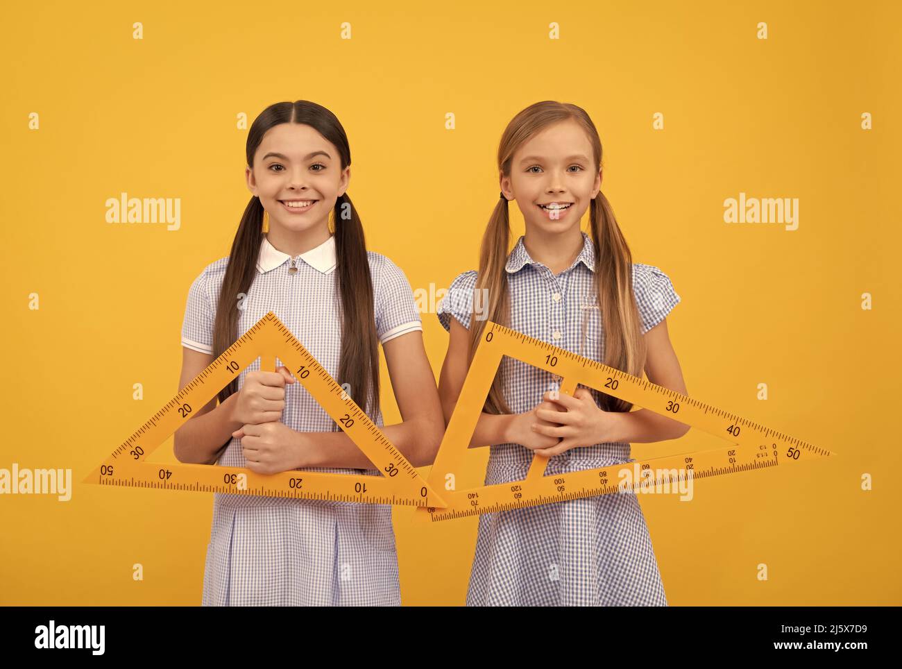 Geometry is for triangles. Happy kids hold triangular rulers. Geometry lesson. School education Stock Photo