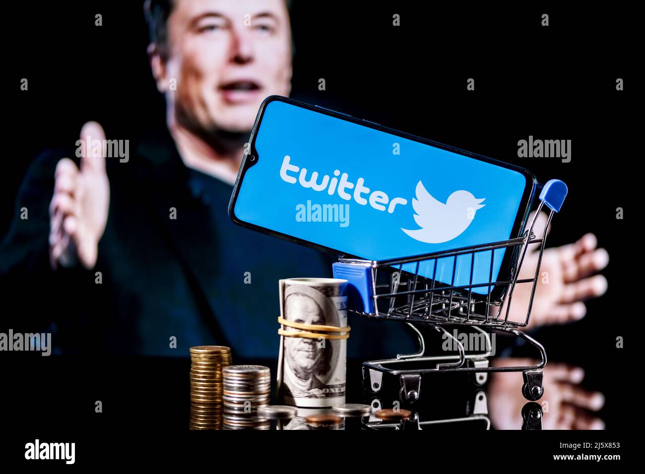 Logo of social network Twitter on smartphone screen in shopping cart with money and photo Elon Musk in background. Stock Photo