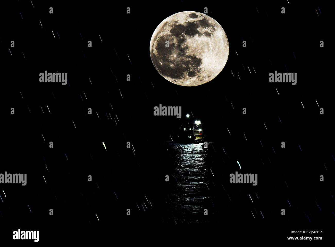 MOONLIGHT TIDE: The moon descends directly above a tugboat as a guiding light in the late night hours in the Atlantic. Stock Photo