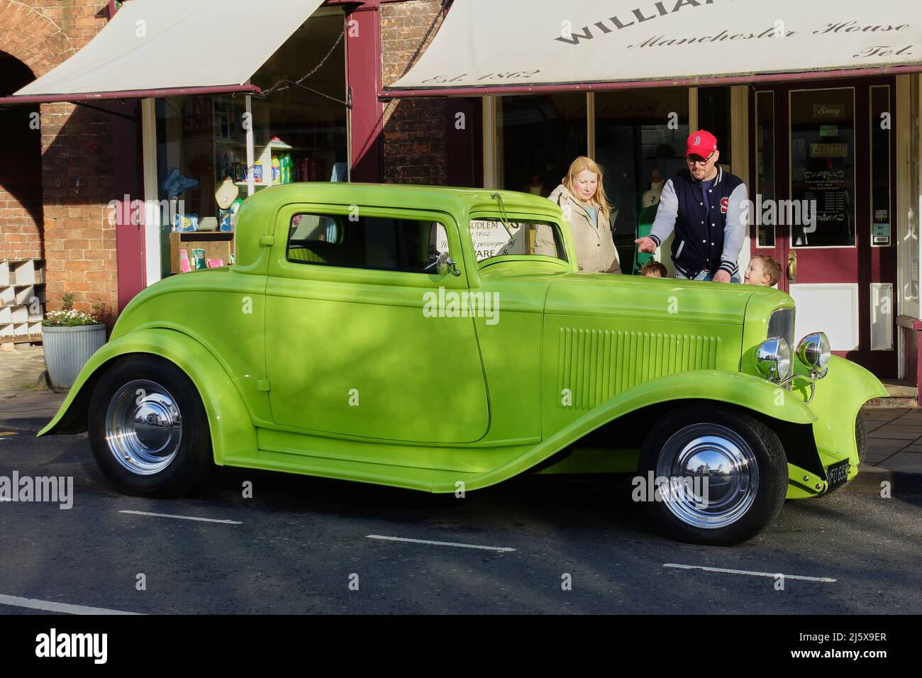 A father showing his wife and children the beauty of a vivid green retro hot-rod parked on the street Stock Photo