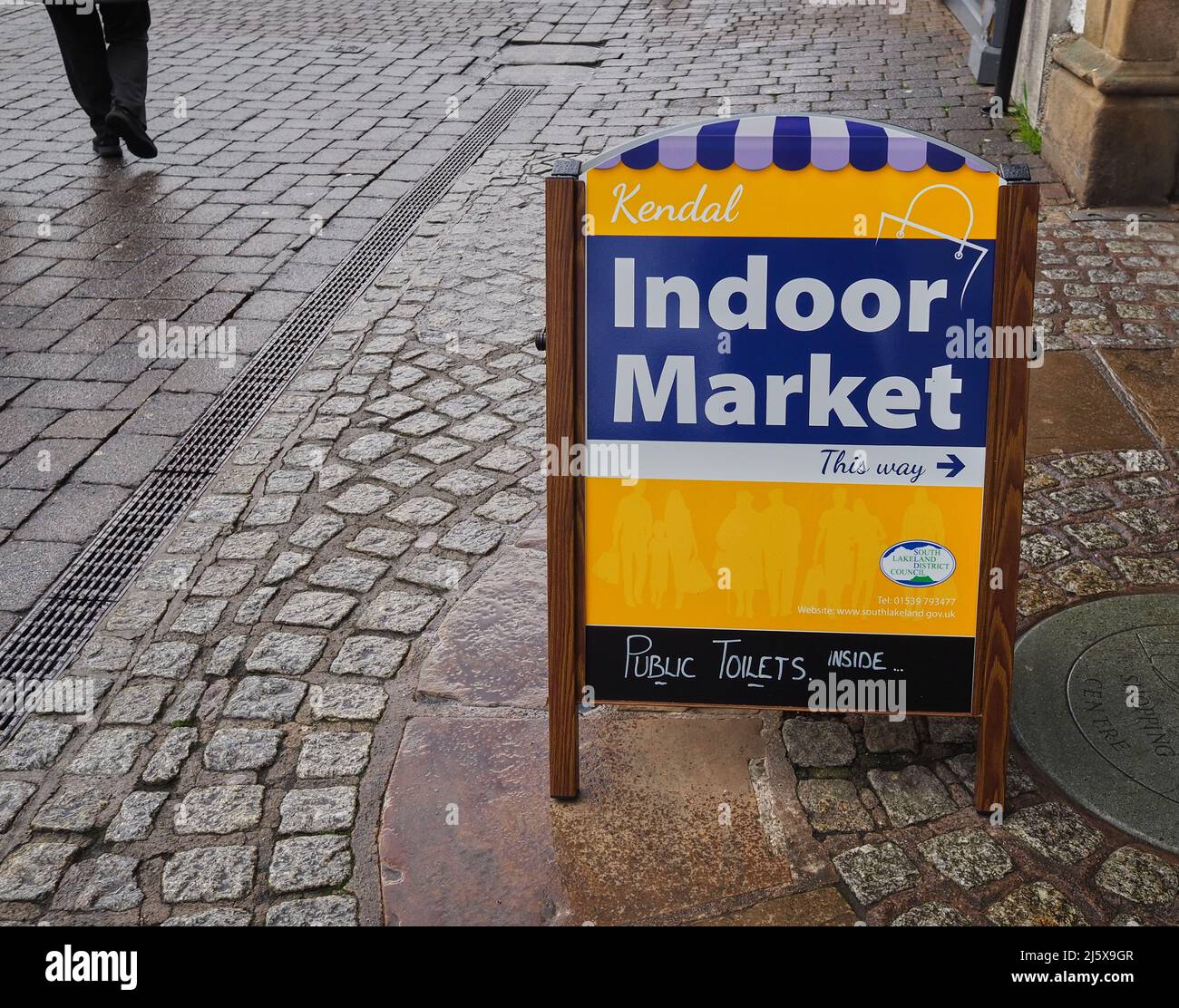 Sign pointing the way to Kendal's indoor market with a persons leg in view just having shopped there Stock Photo