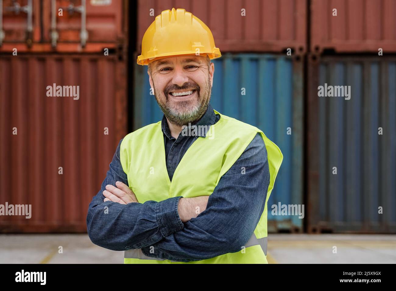 Happy senior man smiling at camera working at industrial shipping freight terminal port - Focus on face Stock Photo