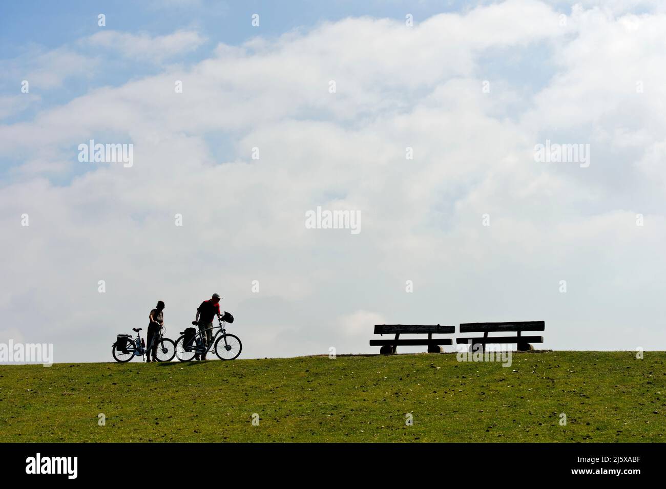 The last few meters, two cyclists push their bikes on a dyke crest to two benches, Schleswig-Holstein Wadden Sea National Park, Westerhever, Schleswig Stock Photo