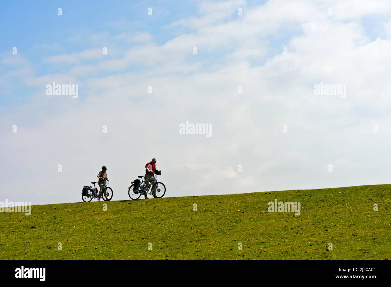 Two cyclists push their bikes on a dyke crest, Schleswig-Holstein Wadden Sea National Park, Westerhever, Schleswig-Holstein, Germany Stock Photo