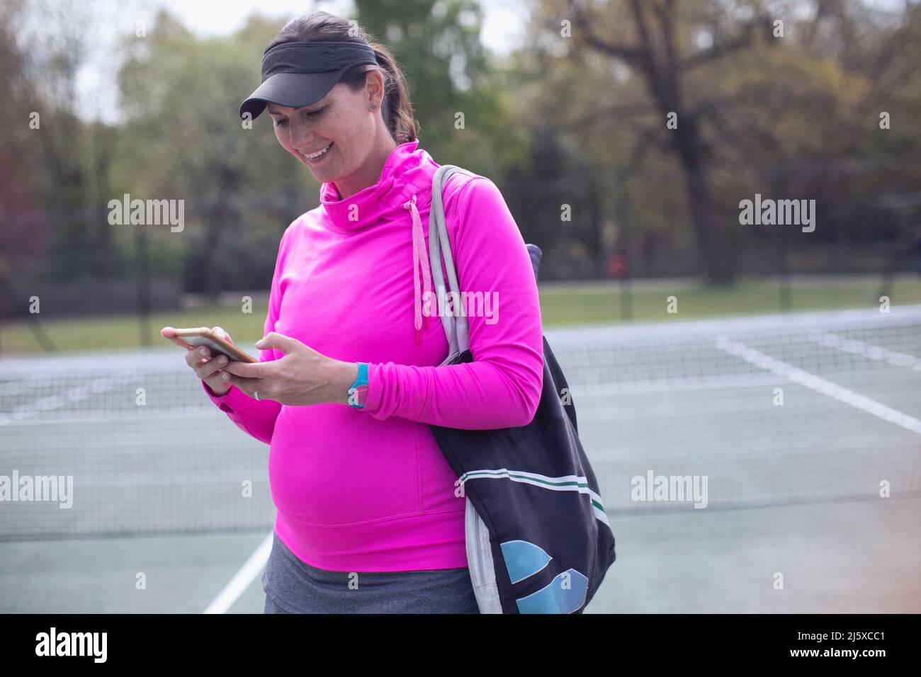 Pregnant woman using smart phone on tennis court Stock Photo