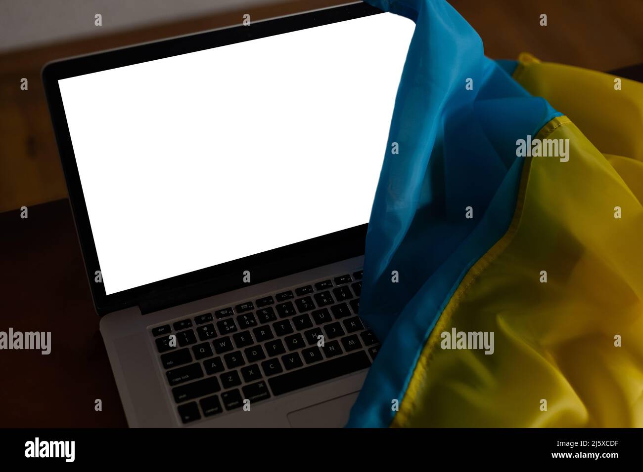 Laptop with blank screen on table and Ukrainian national flag on background, space for text