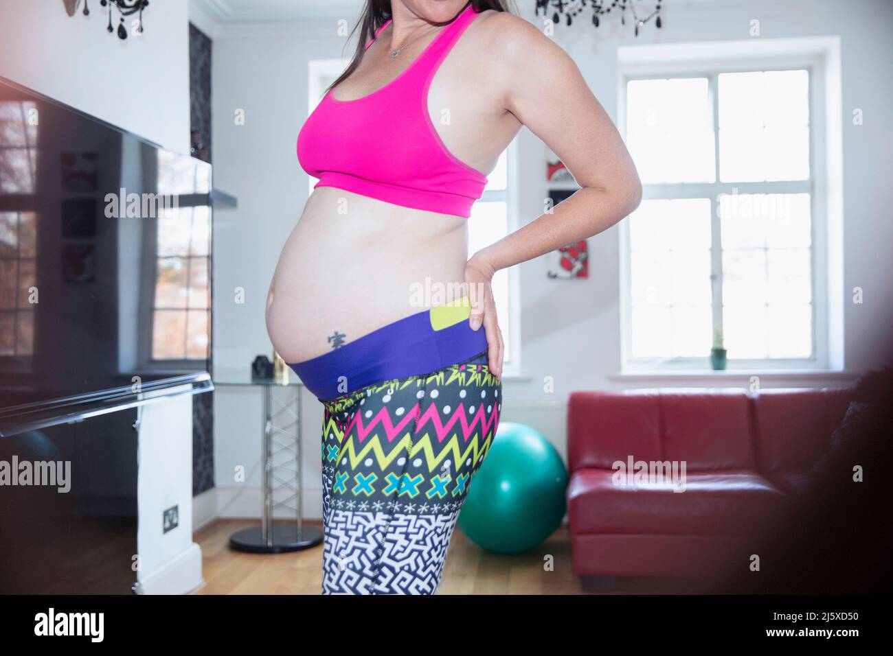 Pregnant woman in sports bra and leggings exercising at home Stock