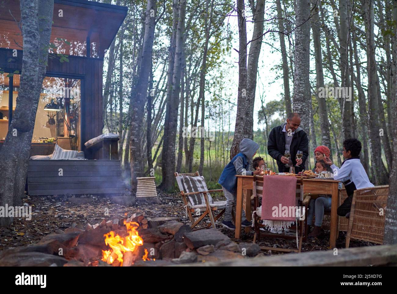 Family enjoying fireside dinner at table in woods outside house rental Stock Photo