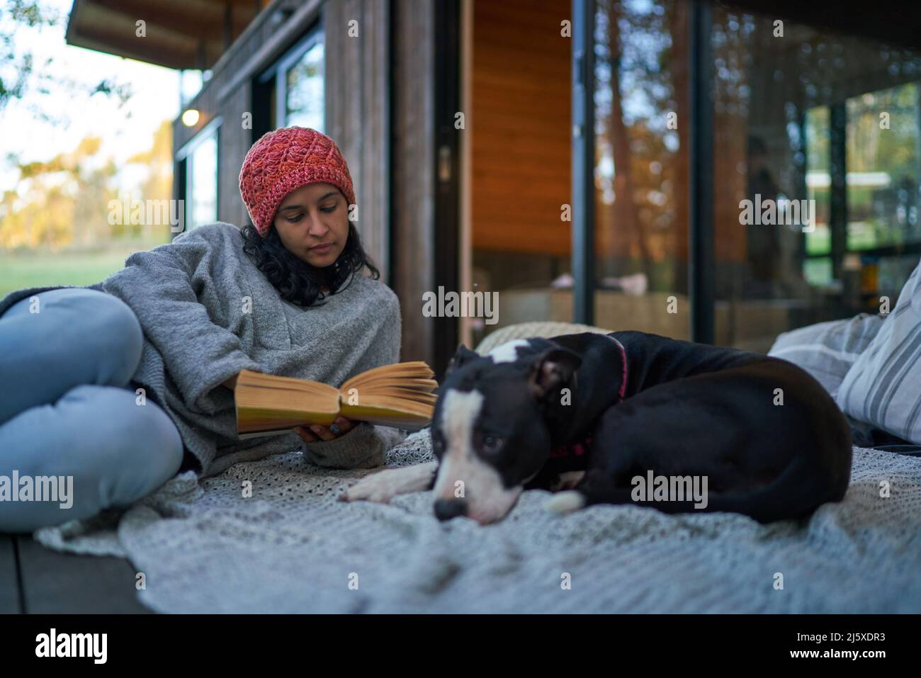Woman reading book next to dog on cabin patio Stock Photo