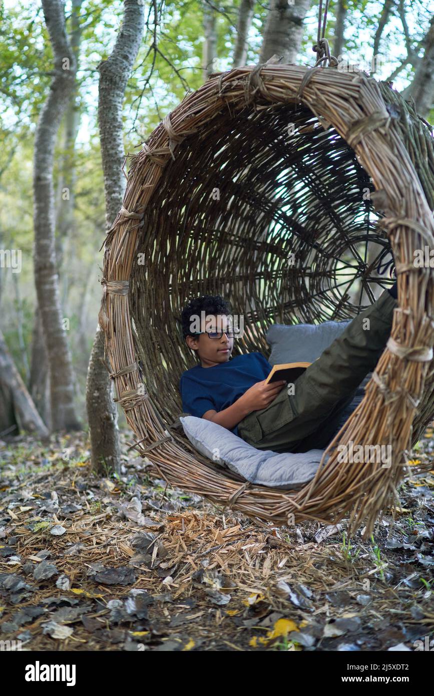 Boy reading book in nest swing in woods Stock Photo