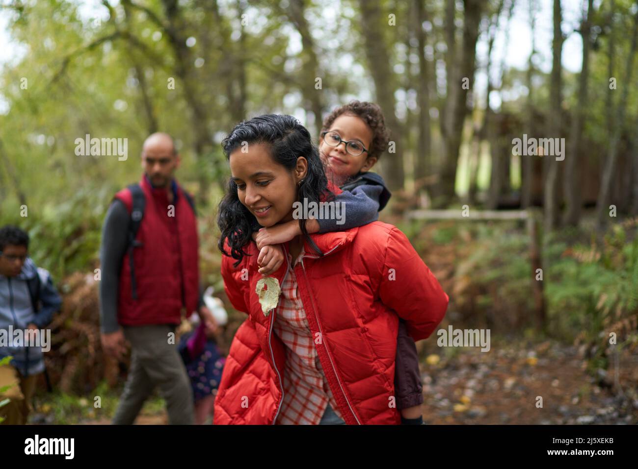 Mother piggybacking son on hike in woods Stock Photo