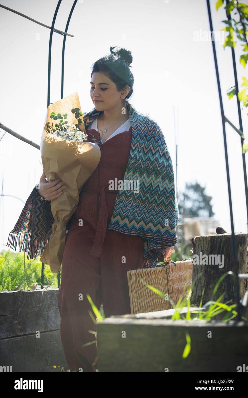 Young woman with bouquet of flowers and picnic basket in sunny garden Stock Photo