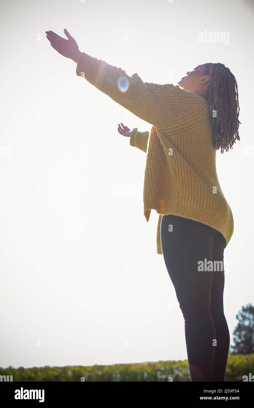 Carefree young woman basking in sunshine with arms outstretched Stock Photo