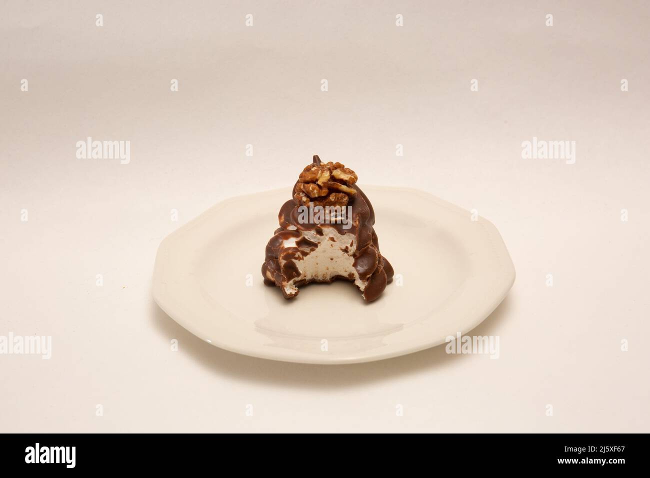 Delicious hand made walnut whip, chocolate covered soft mallow filling  with bite missing on plate isolated on white Stock Photo