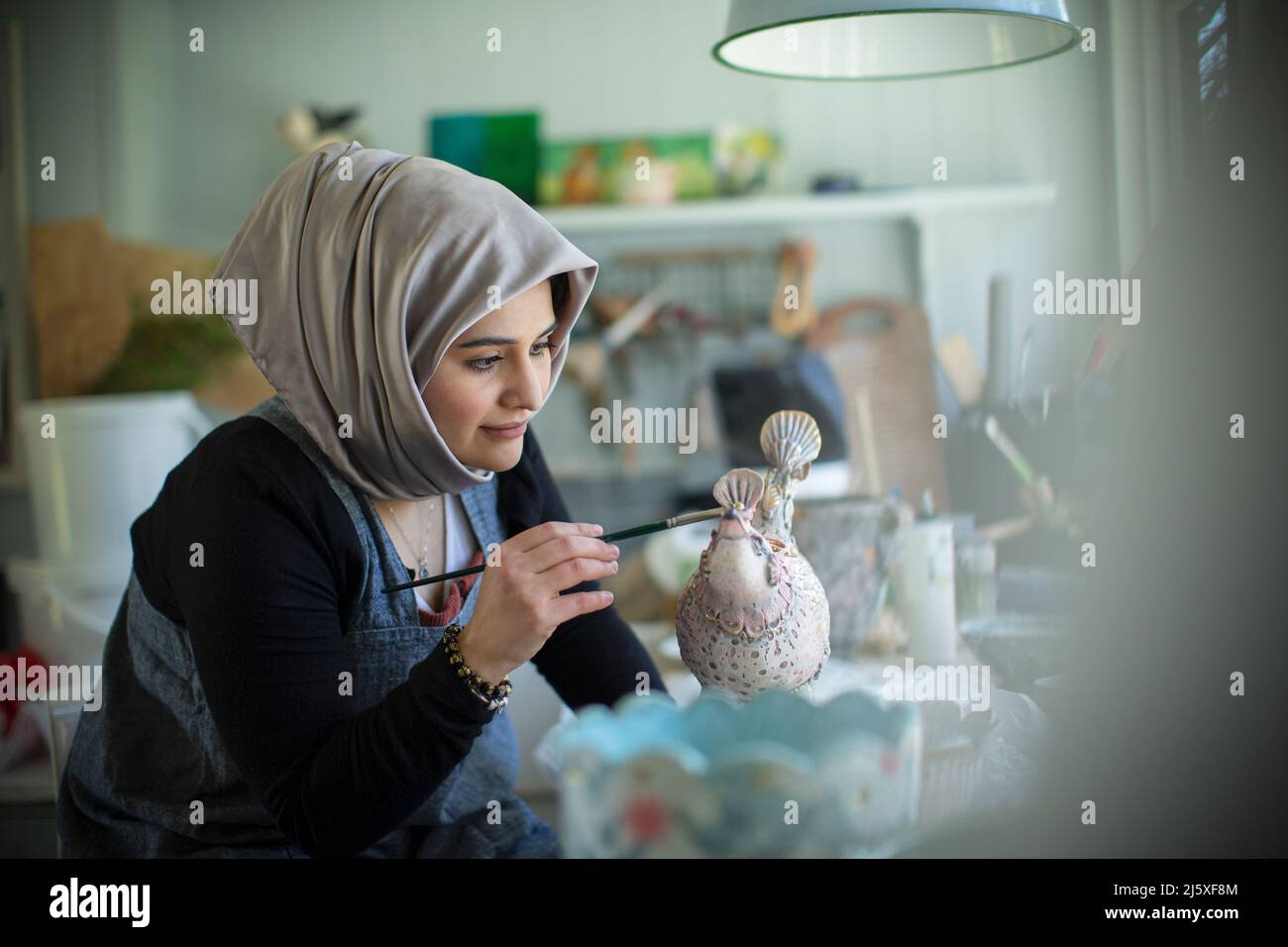 Young Muslim female artist in hijab painting ceramics in art studio