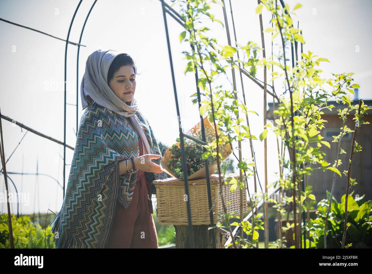 Young Muslim woman with flowers and picnic basket in sunny garden Stock Photo