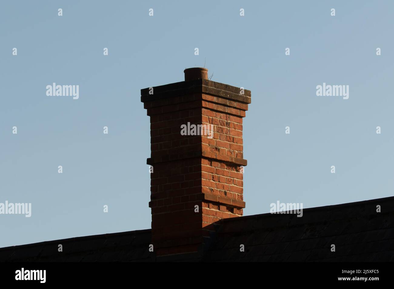 One terracotta chimney pots on weathered Victorian red brick chimney stack and roof against blue sky Stock Photo