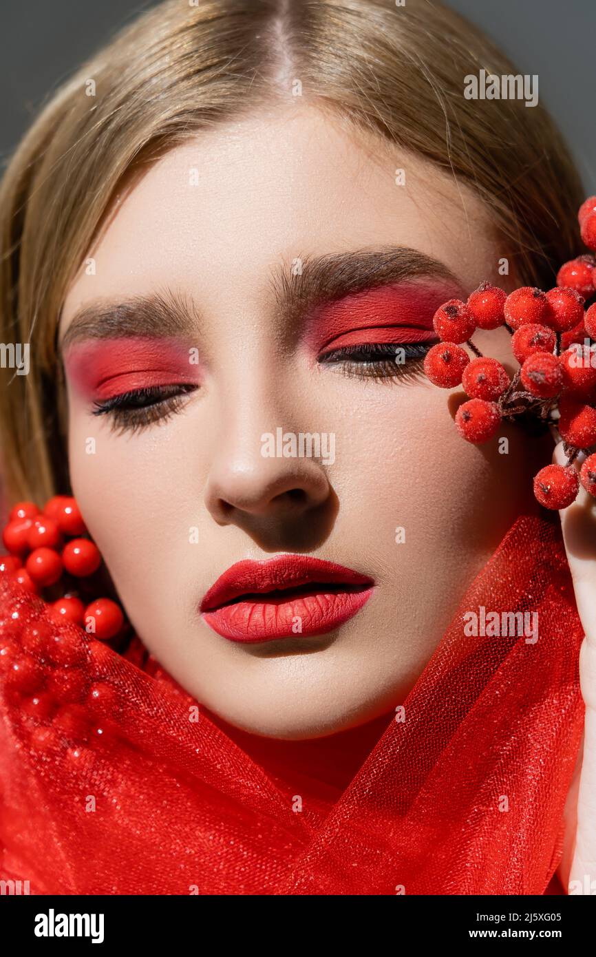 Portrait of pretty model with red visage posing near cloth and berries isolated on grey Stock Photo