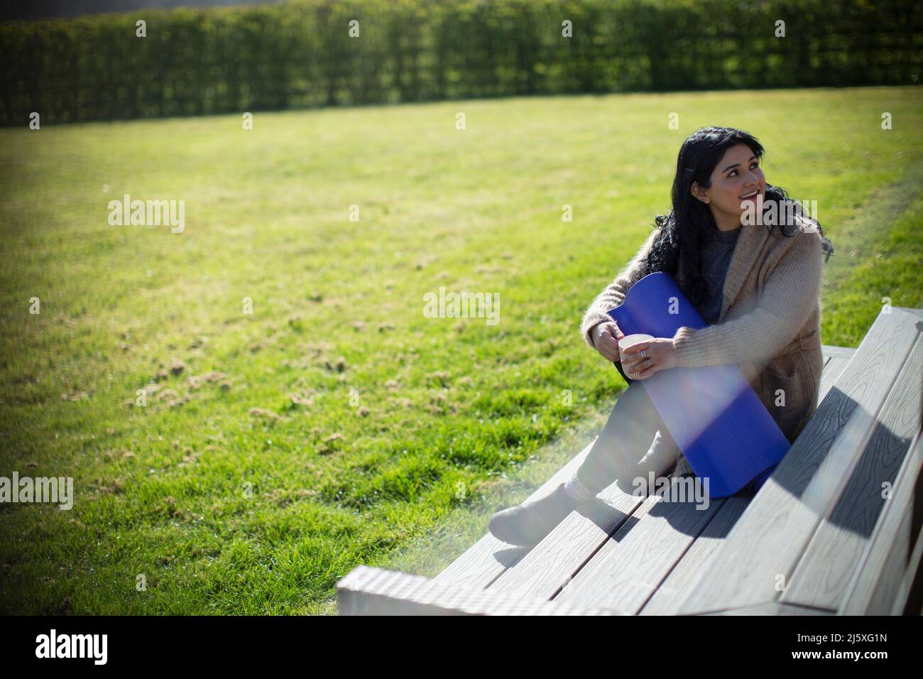 Young woman with yoga mat on sunny park bench Stock Photo