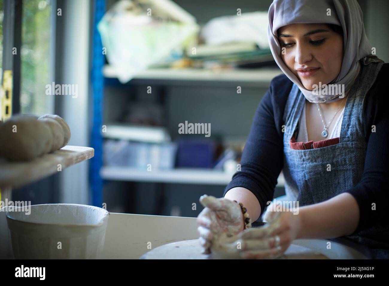 Young female Muslim artist at pottery wheel in art studio Stock Photo