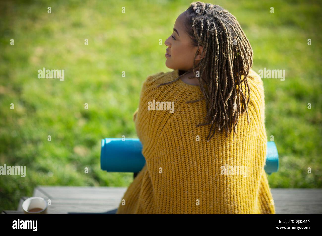Young woman in sweater with yoga mat on sunny patio Stock Photo