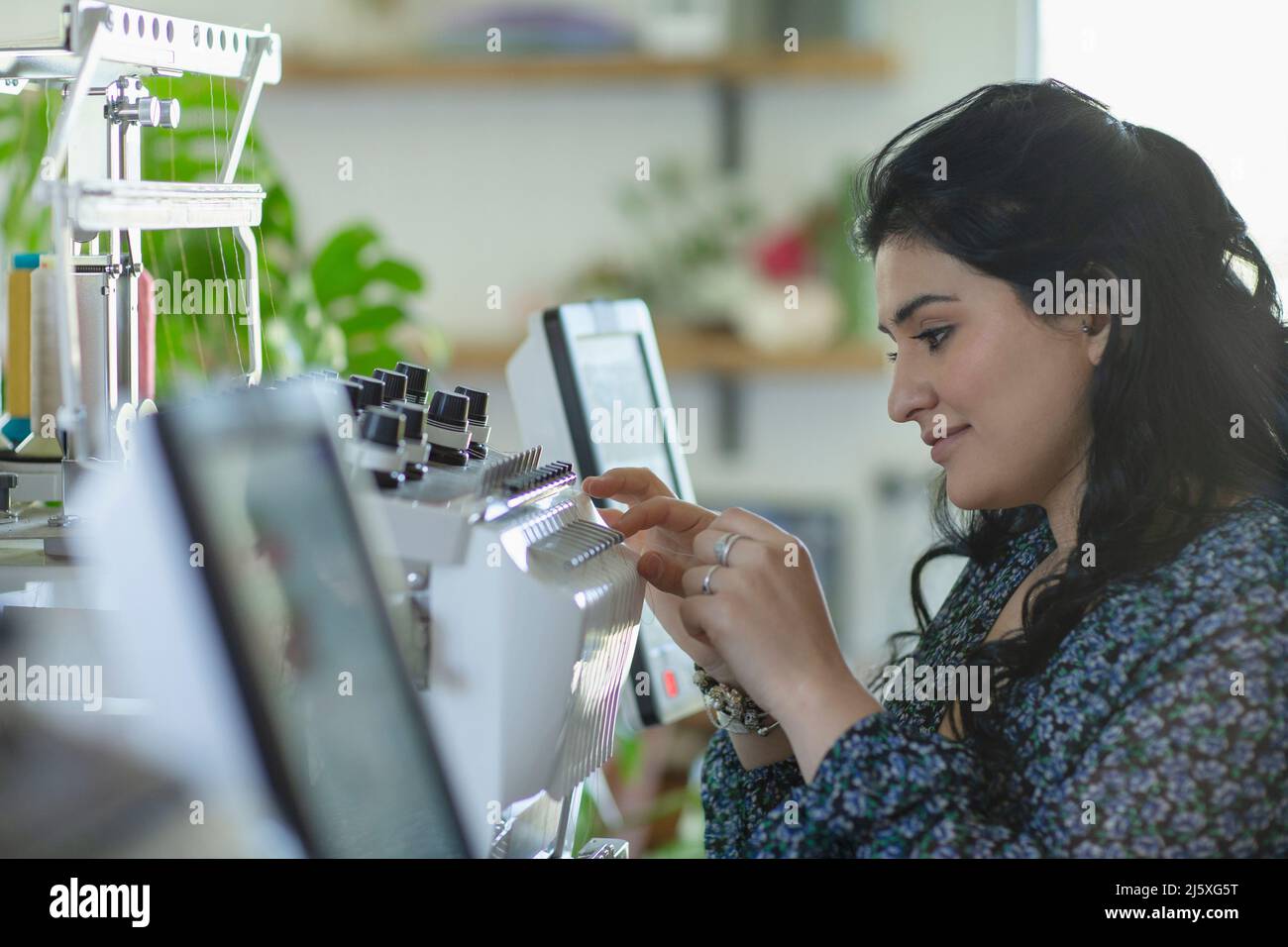 Young female seamstress programming sewing machine in studio Stock Photo