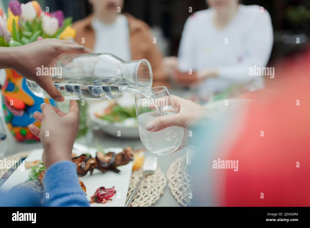 Close up man pouring water from carafe at patio table Stock Photo