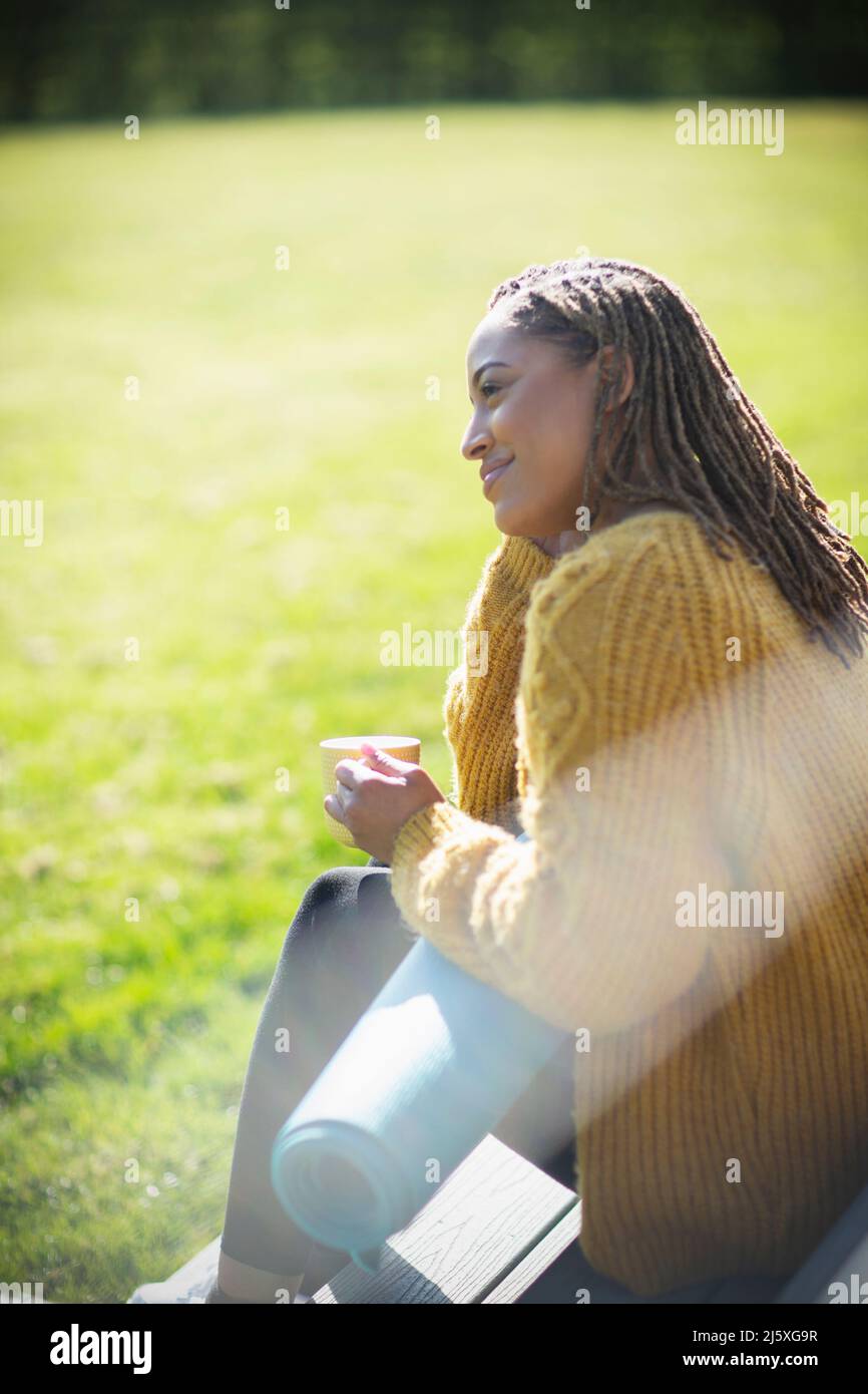 Serene young woman with yoga mat and coffee on sunny patio Stock Photo