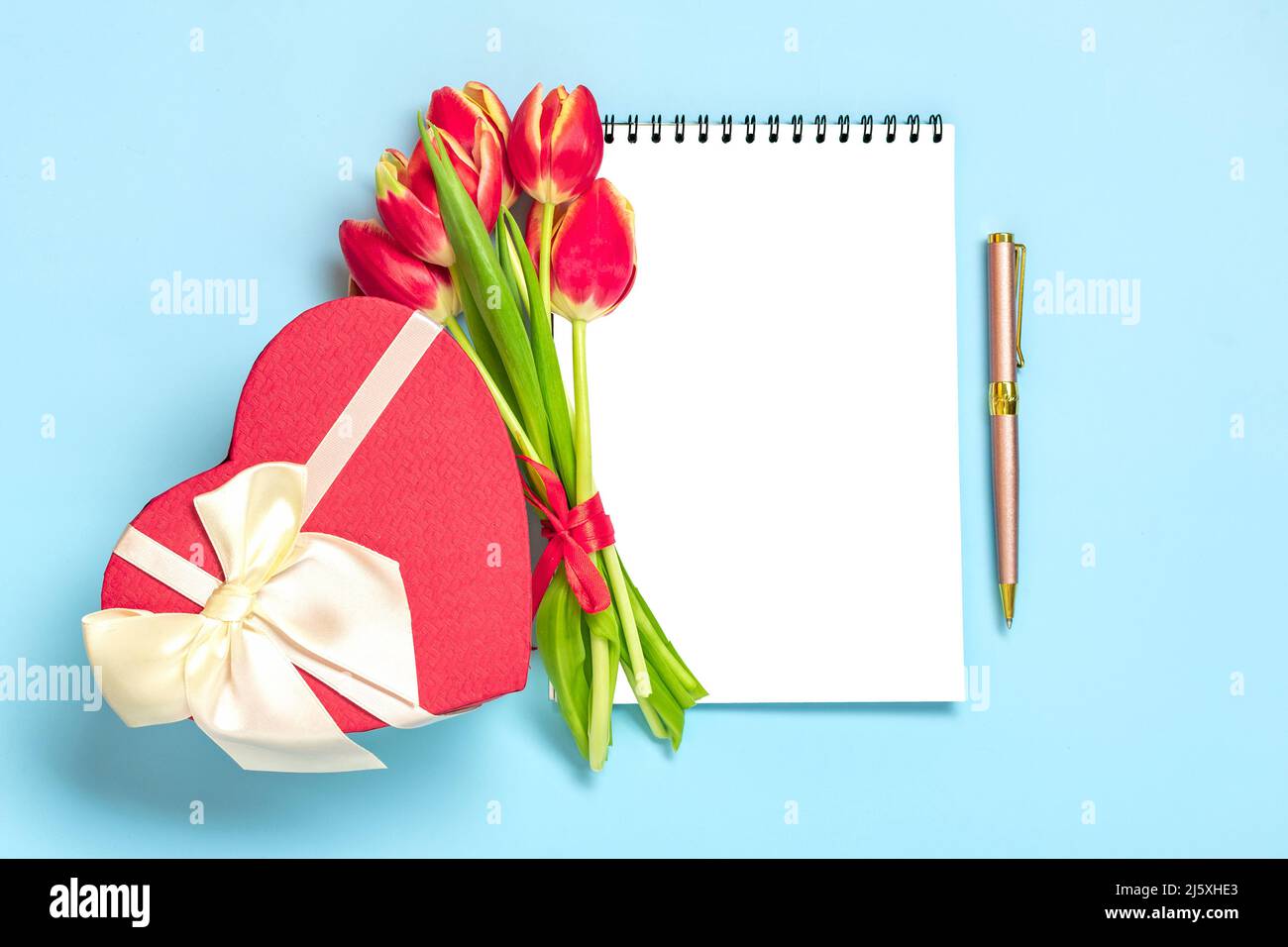 Bouquet of red tulips, gift box heart, notepad on blue background Top view Flat lay Holiday greeting card Happy moter's day, 8 March, Valentine's day, Easter concept Copy space Mock up. Stock Photo