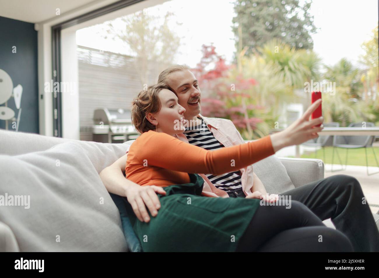 Playful young couple taking selfie with smart phone on sofa Stock Photo