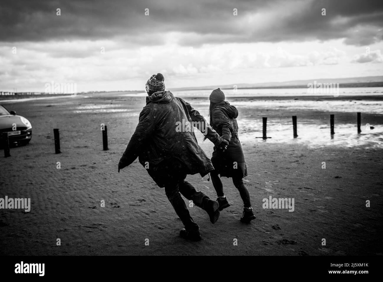 Couple holding hands running on winter beach Stock Photo